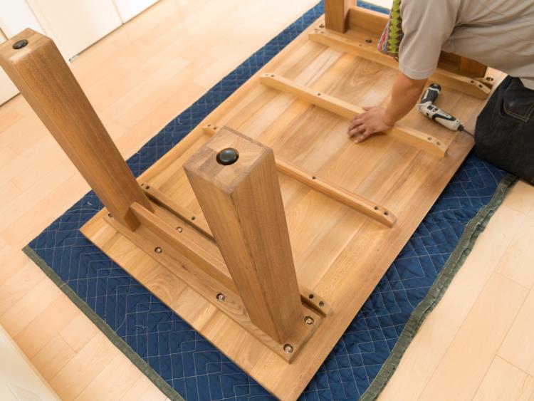 A man tightening screws on a table that is lying upside down on the floor.