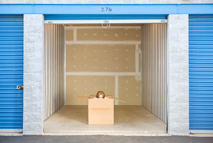 A woman peeking out of a box inside a storage unit.