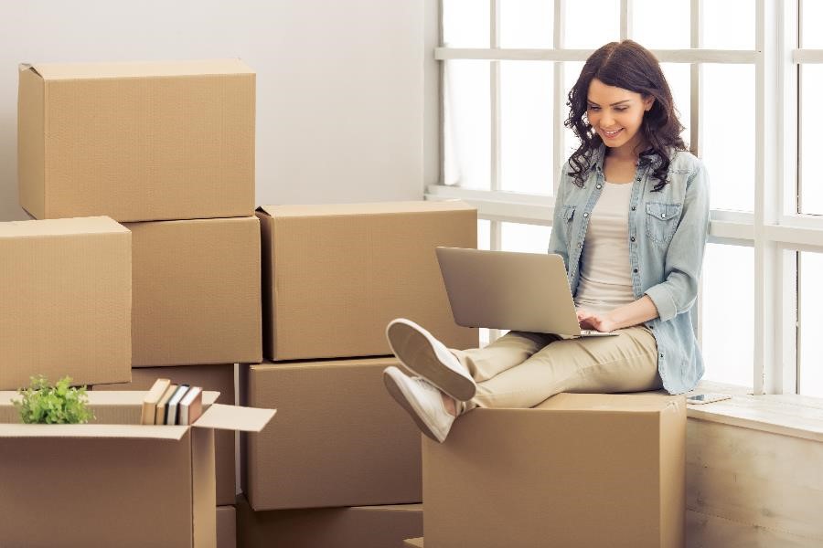Young woman sitting on a pile of cardboard boxes after moving into her new dorm room.