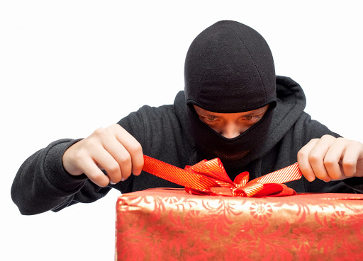 man dressed in black with ski mask attempting to unwrap a Christmas gift