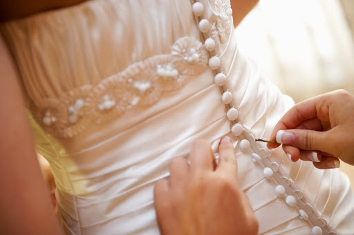 close up of someone pinning the buttons of the back of a wedding dress