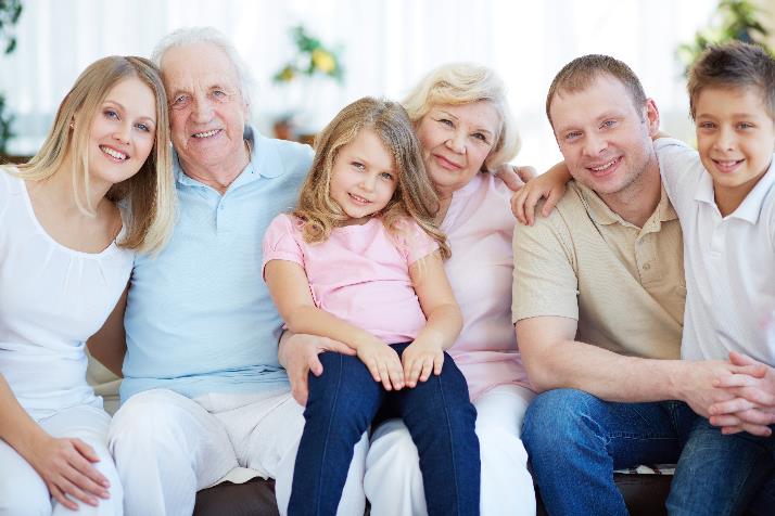 An aging couple smiling and sitting with their adult children and young grandchildren.