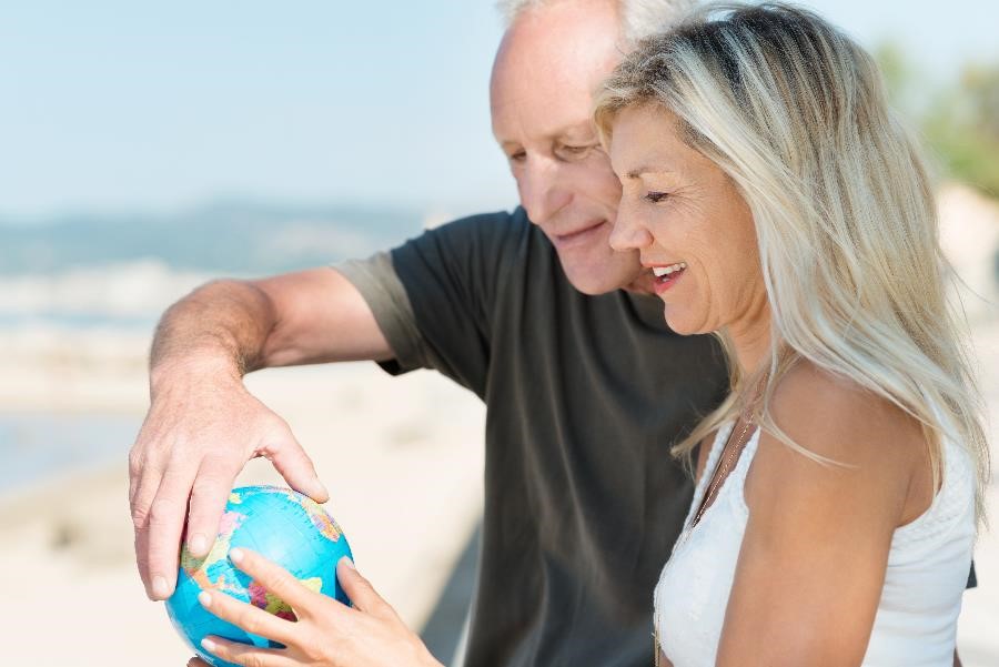 An older retired couple holding a small globe while standing on a Florida beach.