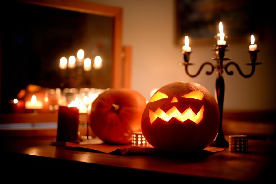 A glowing jack o'lantern sitting next to a lit candelabra in a home's dark dining room.