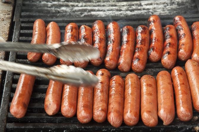 Close-up photo of hot dogs cooking on a grill.