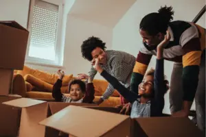 A man in woman smiling while two kids play in moving boxes
